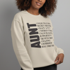 A woman smiling while wearing a cream-colored Gildan 18000 crewneck sweatshirt featuring a large vertical "AUNT" graphic and a witty list of definitions in black typography.